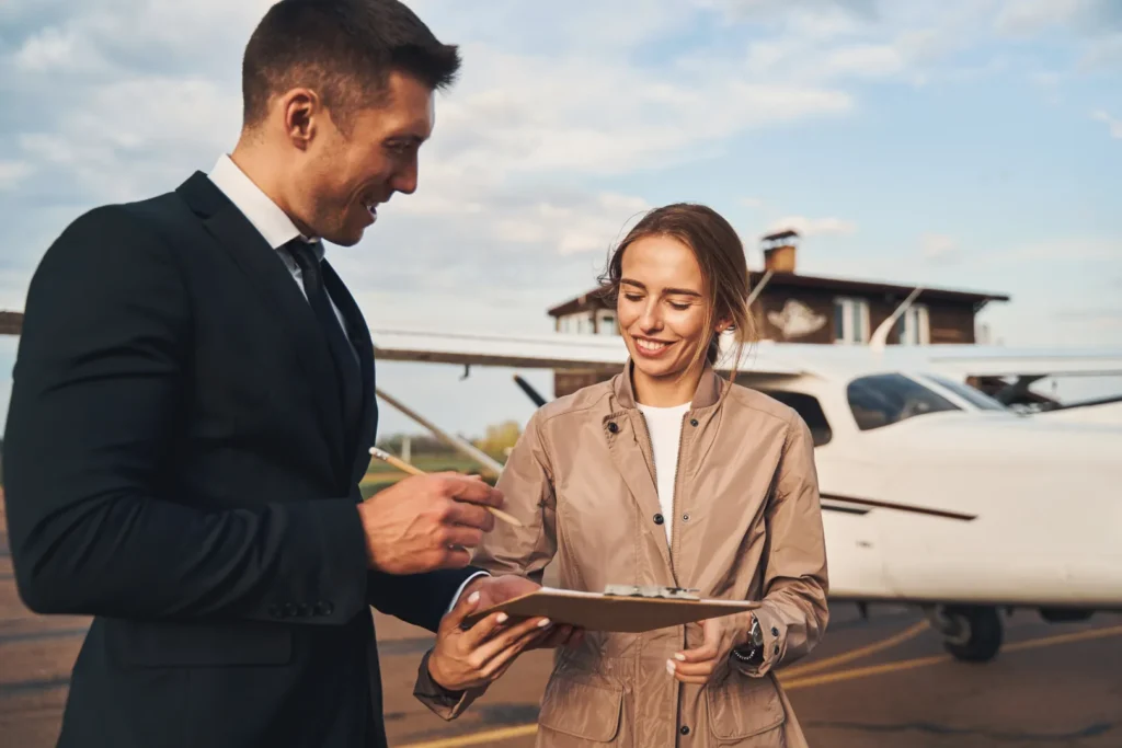 Businessman and woman discussing private jet charter details beside a private aircraft at an airport.