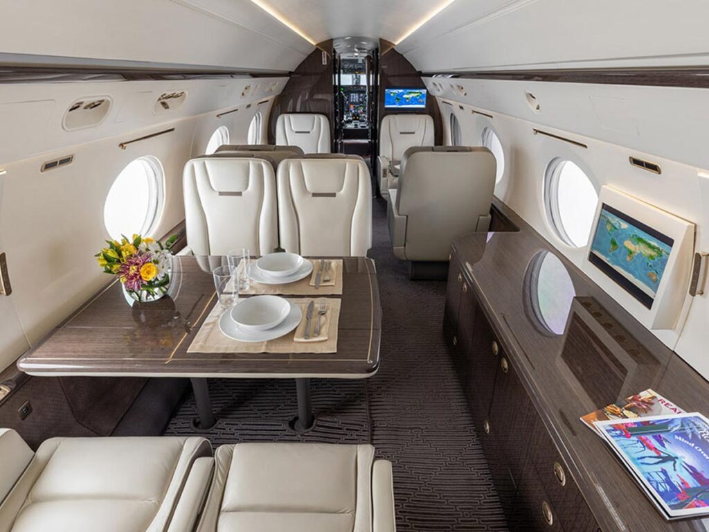 Private jet cabin interior with cream leather seats, a dining table, and luxury finishes.